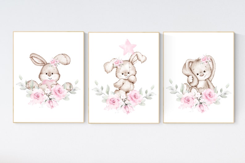 May include: Three watercolor illustrations of bunnies with pink flowers. Each bunny is brown with a pink nose and pink flowers in their fur. The background is white.
