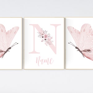 May include: Three framed prints with a pink watercolor butterfly on each side and a pink letter N with floral accents in the center. The letter N is decorated with pink flowers and leaves. The text "Name" is written below the letter.