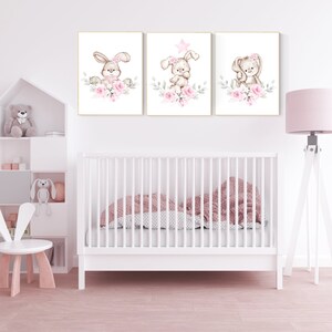 May include: Three framed prints with watercolor illustrations of bunnies with pink flowers. The bunnies are wearing pink bows and have a star on their heads. The prints are hung on a white wall above a white crib.