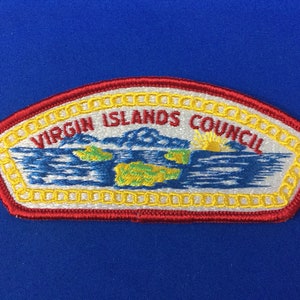 May include: A white and red embroidered patch with a yellow border. The patch features a blue and white image of three islands with a yellow sun rising over them. The text "VIRGIN ISLANDS COUNCIL" is written in white on the patch.