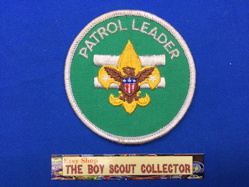 Puede incluir: Un parche de l&iacute;der de patrulla de Boy Scout bordado en verde y blanco con una flor de lis dorada y las palabras "Patrol Leader" en blanco.