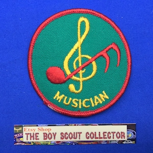 Op de afbeelding: Een geborduurde patch in groen en rood met een gele vioolsleutel en een rode noot. De tekst "MUSICIAN" is in geel onder de noten geborduurd.