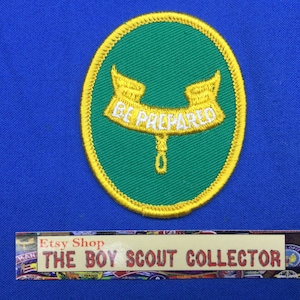 May include: A green and gold embroidered patch with the words "BE PREPARED" on a banner. The patch is oval-shaped and set against a blue background. The Etsy shop name "THE BOY SCOUT COLLECTOR" is at the bottom.