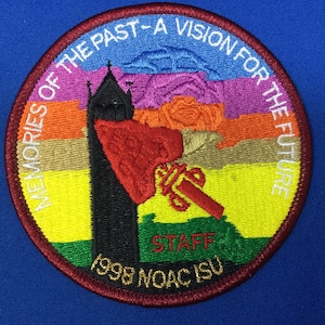 Puede incluir: Un parche redondo bordado con un esquema de color rojo, blanco y azul. Presenta una imagen estilizada de un edificio con una rosa y el texto "Memories of the Past - A Vision for the Future". La parte inferior del parche dice "1998 NOAC ISU Staff".
