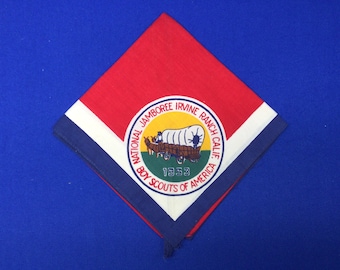 Può includere: Un fazzoletto da collo dei Boy Scouts of America di colore rosso, bianco e blu con una toppa circolare che recita "National Jamboree Irvine Ranch Calif. 1953 Boy Scouts of America". La toppa presenta un carro giallo su sfondo verde.