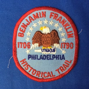 May include: A blue and red embroidered patch with a bald eagle, stars, and the text "Benjamin Franklin 1706 - 1790 Philadelphia Historical Trail".