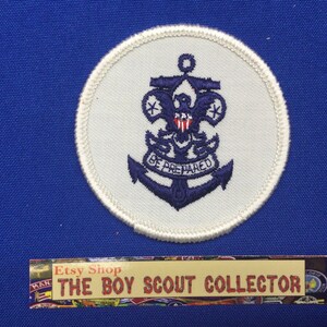 Könnte beinhalten: Runder Aufnäher mit einem marineblauen Ankerdesign auf weißem Grund. Das Design umfasst einen Adler, das Pfadfinder-Emblem und die Worte "BE PREPARED". Der Aufnäher befindet sich auf blauem Hintergrund.