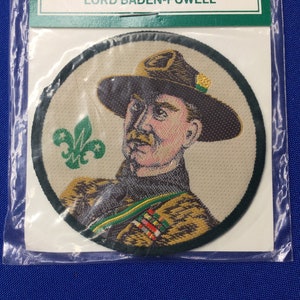 Könnte beinhalten: Ein runder gestickter Aufnäher mit einem Porträt von Lord Baden-Powell, dem Gründer der Pfadfinder, der einen Pfadfinderhut trägt. Der Aufnäher ist von einem grünen Rand umgeben und zeigt ein grünes Pfadfinderemblem.