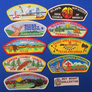 Op de afbeelding: Een verzameling geborduurde Boy Scout-patches met verschillende radenamen en afbeeldingen. Ontwerpen omvatten een brug, hert, bizon en een raketlancering. De patches zijn in verschillende kleuren en vormen.