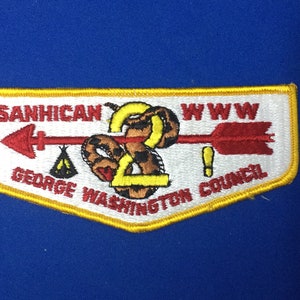 Puede incluir: Un parche blanco bordado con un borde amarillo. El parche presenta una flecha roja con una serpiente envuelta alrededor. El texto "SANHICAN 2 WWW GEORGE WASHINGTON COUNCIL" está bordado en el parche.