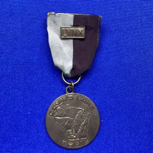 Puede incluir: Una medalla vintage con una cinta que presenta el texto "LYNX" en una pequeña barra rectangular. La medalla tiene un diseño circular con las palabras "DEVIL'S LAKE TRAIL" y una representación de un mapa. La cinta está rayada con blanco y granate oscuro.