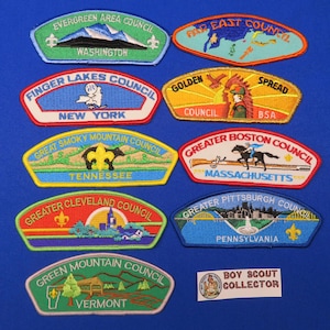 May include: A collection of Boy Scout patches featuring various council emblems. The patches display colorful designs with text indicating the council name and state, such as "Evergreen Area Council, Washington" and "Greater Boston Council, Massachusetts."