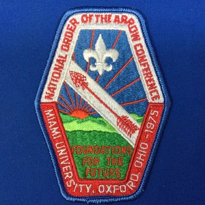 Puede incluir: Parche bordado con borde rojo y diseño azul, blanco y verde. El parche presenta el texto "National Order of the Arrow Conference" y "Foundations for the Future". El parche también incluye una flor de lis y una flecha.