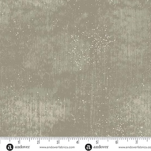 May include: A fabric with a textured, mottled appearance in shades of gray and beige. The design features vertical streaks and scattered white speckles, creating a distressed, industrial aesthetic. The bottom edge displays a ruler with inch measurements.
