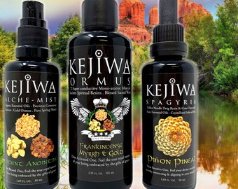 Puede incluir: Tres botellas negras de productos Kejiwa, incluyendo Alche-Mist, Ormus y Spagyria. Cada botella tiene una etiqueta única con texto e ilustraciones. El fondo muestra una vista panorámica de un lago y montañas.