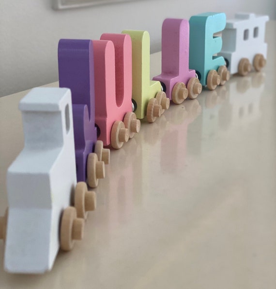 A custom wooden name train puzzle in pastel colors where each car is a letter of the child's name — genuinely charming Montessori-style toy with a massive 449-favorite demand signal.