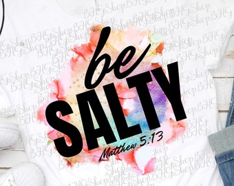 May include: A white t-shirt with a watercolor design featuring a rainbow of colors. The design includes the text "be SALTY" in black with the scripture reference "Matthew 5:13" underneath.
