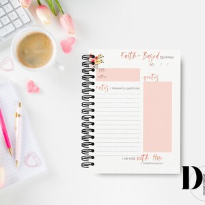 May include: A pink and white journal with a floral design on the cover. The journal is titled "Faith-Based Reading" and has sections for notes, thoughts, questions, and quotes. The journal also includes the scripture "I am one with Him - 1 Corinthians 6:17".