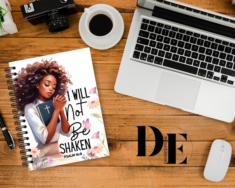 May include: A white spiral notebook with a colorful illustration of a woman with her hands clasped in prayer. The text "I WILL NOT BE SHAKEN" is printed in black with the scripture reference "PSALM 16:8" below. The background features pink and purple flowers.