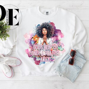 May include: White sweatshirt with a watercolor design of a woman praying with butterflies and flowers. The text "God's help is only a prayer away" is printed on the sweatshirt.