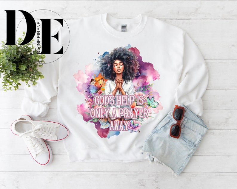 May include: White sweatshirt with a watercolor design of a woman praying with butterflies and flowers. The text "God's help is only a prayer away" is printed on the sweatshirt.