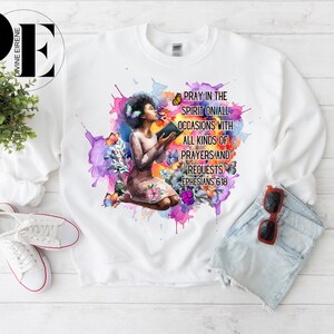 May include: White sweatshirt with a watercolor design of a woman praying with a book. The design includes butterflies and the text "Pray in the Spirit on all occasions with all kinds of prayers and requests Ephesians 6:18".