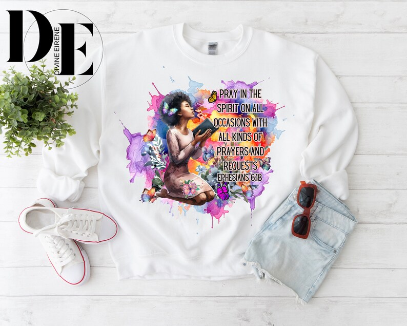 May include: White sweatshirt with a watercolor design of a woman praying with a book. The design includes butterflies and the text "Pray in the Spirit on all occasions with all kinds of prayers and requests Ephesians 6:18".