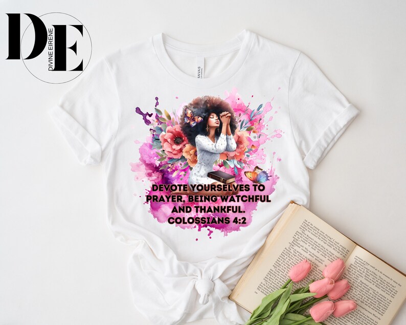 May include: White t-shirt with a watercolor design of a woman praying with flowers and butterflies. The text on the shirt reads "Devote yourselves to prayer, being watchful and thankful. Colossians 4:2"