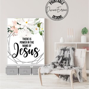 May include: A printable wall art design with a white background and a floral design in the top left corner. The text "There is power in the name of Jesus" is written in black lettering.