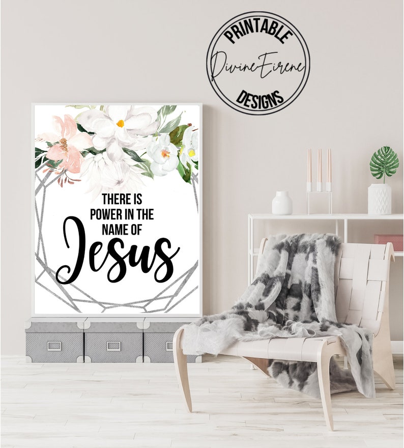 May include: A printable wall art design with a white background and a floral design in the top left corner. The text "There is power in the name of Jesus" is written in black lettering.