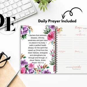 May include: A pink and purple floral design journal with a daily prayer included. The journal has a spiral binding and a section for prayer requests, confessions, and thanks. The text on the cover reads "God is my provider, Philippians 4:19".