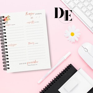 May include: A pink and white prayer journal with a floral design on the cover. The journal has a spiral binding and is divided into sections for prayer requests, confessions, and thanks. The text on the cover reads "Prayer Journal" and "God is my provider, Philippians 4:19".