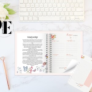 May include: A pink and white prayer journal with a floral design on the cover. The journal has a spiral binding and includes sections for prayer requests, praise, confession, and thanks. The journal also includes a reflection page with a floral design and the text "I am the light".