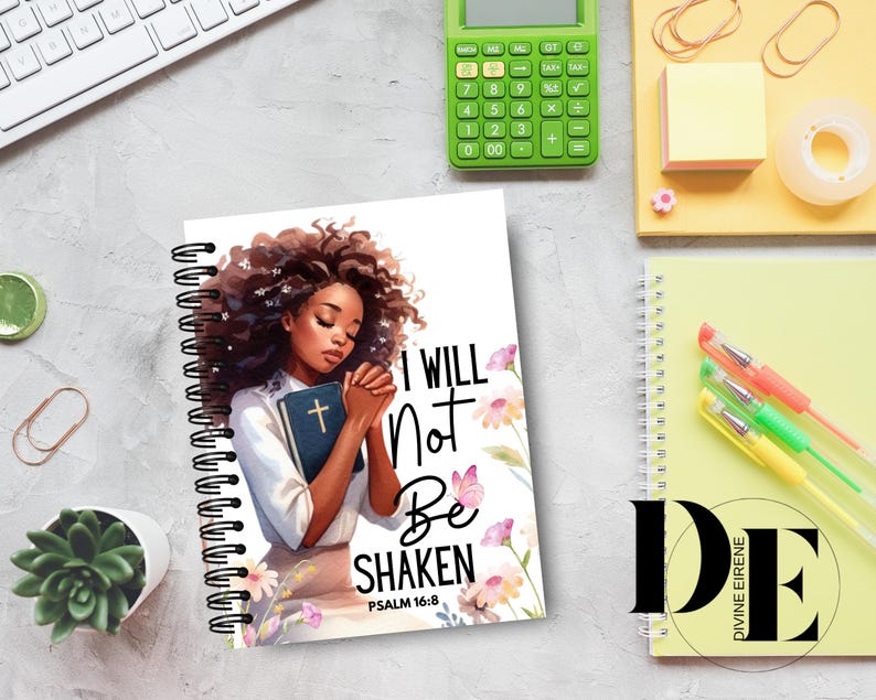 May include: A spiral bound notebook with a white cover featuring a black woman with brown hair, holding a bible. The cover has a floral design and the text "I will not be shaken Psalm 16:8".
