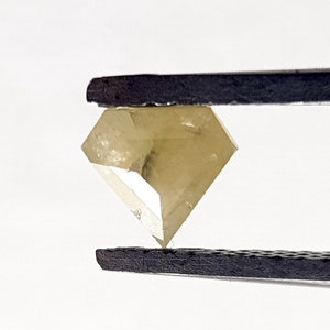 Puede incluir: Un diamante amarillo claro y facetado sostenido por unas pinzas.