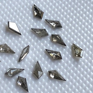 May include: A collection of 14 gray diamond shaped gemstones on a white textured surface.