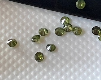 May include: A collection of small, faceted, green gemstones on a white textured surface.