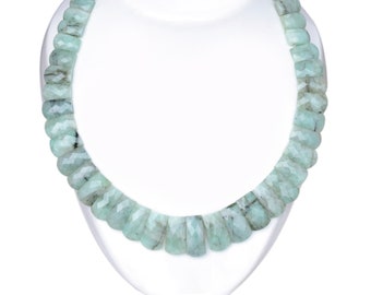 May include: A necklace made of light green emerald beads. The beads are faceted and have a slightly irregular shape. The necklace is displayed on a white mannequin.