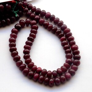 May include: A strand of deep red ruby beads, each bead is round and smooth. The beads are strung on a clear thread and are arranged in a double strand.