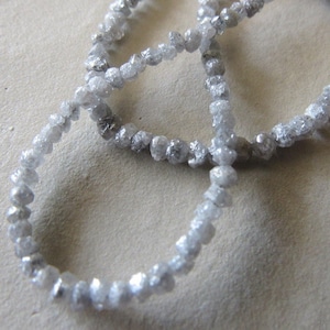 May include: A strand of rough, unpolished, gray diamonds strung together as a necklace. The diamonds are small and irregular in shape.