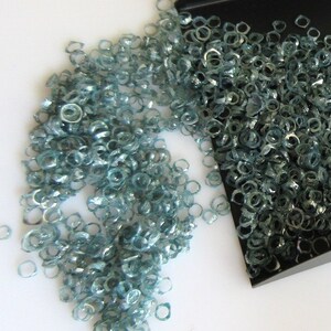 May include: A black tray with a pile of light blue, faceted, gemstone rings spilling out onto a white surface.
