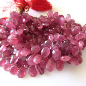 May include: A strand of pink gemstone beads. The beads are oval shaped and have a faceted finish.