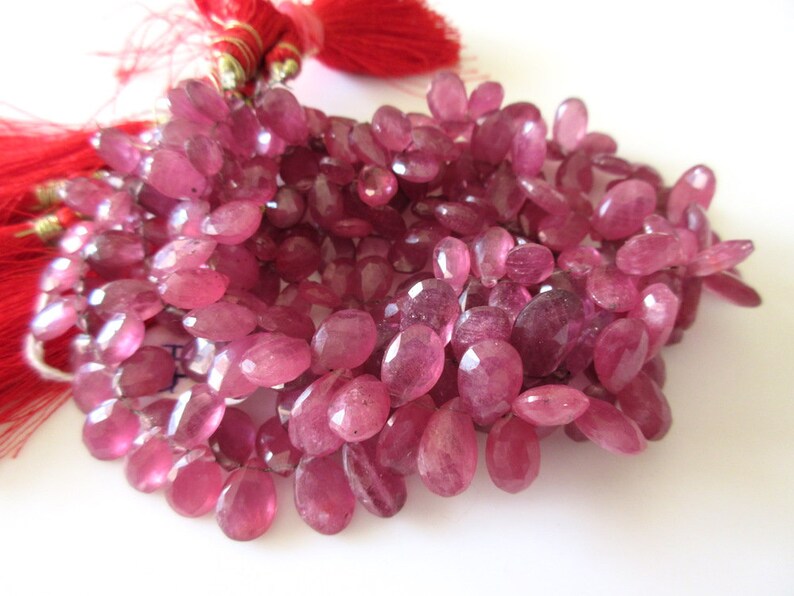 May include: A strand of pink gemstone beads. The beads are oval shaped and have a faceted finish.