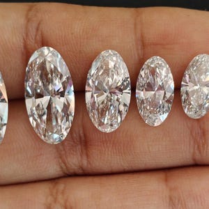 May include: Five clear, colorless, oval-cut gemstones arranged in a row by size from largest to smallest. Each stone features a faceted surface that reflects light, creating a brilliant, sparkling appearance with sharp, pointed ends and rounded sides.