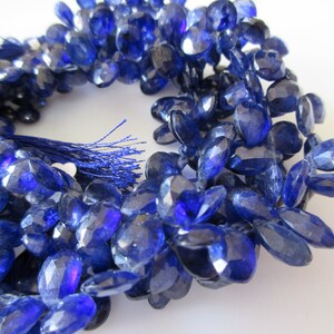 May include: A strand of blue gemstone beads, each bead is faceted and oval shaped. The beads are strung on a cord with a tassel at the end.