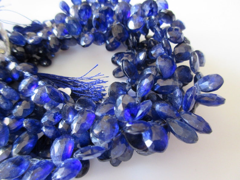 May include: A strand of blue gemstone beads, each bead is faceted and oval shaped. The beads are strung on a cord with a tassel at the end.
