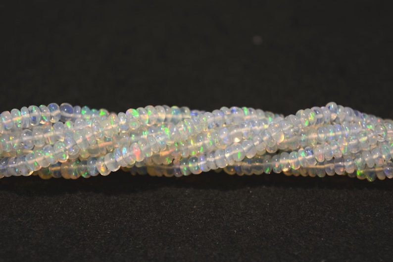 May include: A strand of white opal beads with iridescent flashes of color. The beads are round and smooth, and they are strung on a clear thread.
