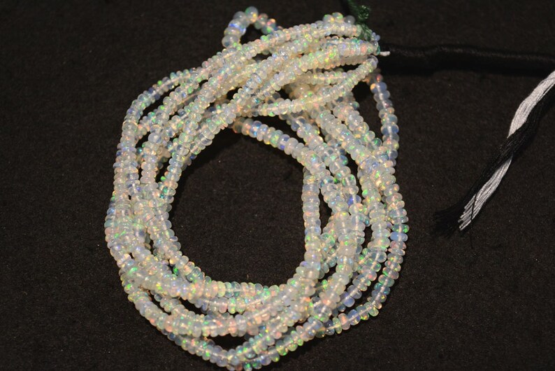 May include: A strand of white opal beads, with iridescent rainbow flashes, strung on a black cord. The beads are small and round, and the strand is long enough to be worn as a necklace or bracelet.
