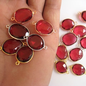 May include: A collection of 12 oval-shaped red gemstone connectors with gold-toned metal accents. The connectors have a smooth, polished finish and are perfect for jewelry making.