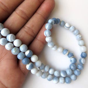 May include: A strand of blue and white opal beads. The beads are round and have a smooth, polished finish. The beads are strung on a clear elastic cord.